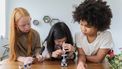 Drie kinderen die in een microscoop kijken