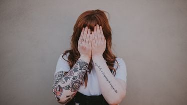 vrouw met tattoos en handen voor haar gezicht