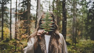 vrouw in het bos met een groen blad in haar hand