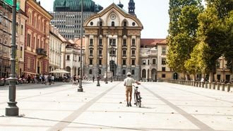 man loopt met fiets aan de hand over plein in Ljubljana.