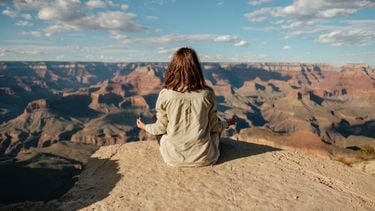 Vrouw die op een berg mediteert, met haar rug naar de camera