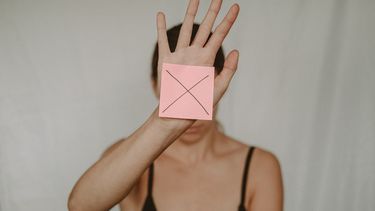 vrouw houdt post-it met kruis voor haar gezicht