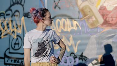 Vrouw met gekleurd haar staat voor een muur met graffiti