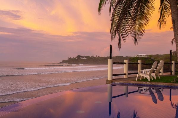 infinity pool met ligbed en palmbomen tijdens zonsondergang