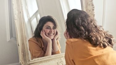 Vrouw die naar zichzelf kijkt in de spiegel