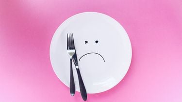 zilveren mes en vork op wit bord met droevige smiley