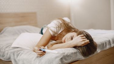 vrouw ligt op bed met zwangerschapstest