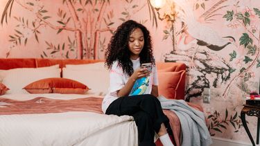 FOMO social media, persoon zit op bed en kijkt op telefoon
