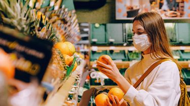 Vrouw met mondkapje in de supermarkt bij het fruit