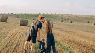 Man en vrouw met klein kindje kussen in veld met hooibalen