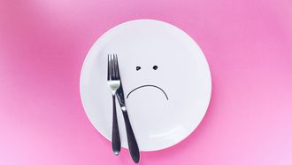 zilveren mes en vork op wit bord met droevige smiley
