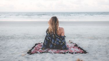 vrouw alleen op een kleedje op het strand
