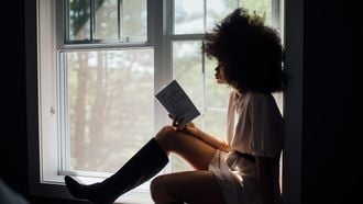 Vrouw die met een boek voor het raam zit te lezen