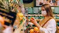 Vrouw met mondkapje in de supermarkt bij het fruit